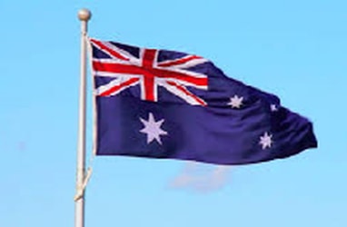 Australian flag on a mast billowing against a blue sky with cloud