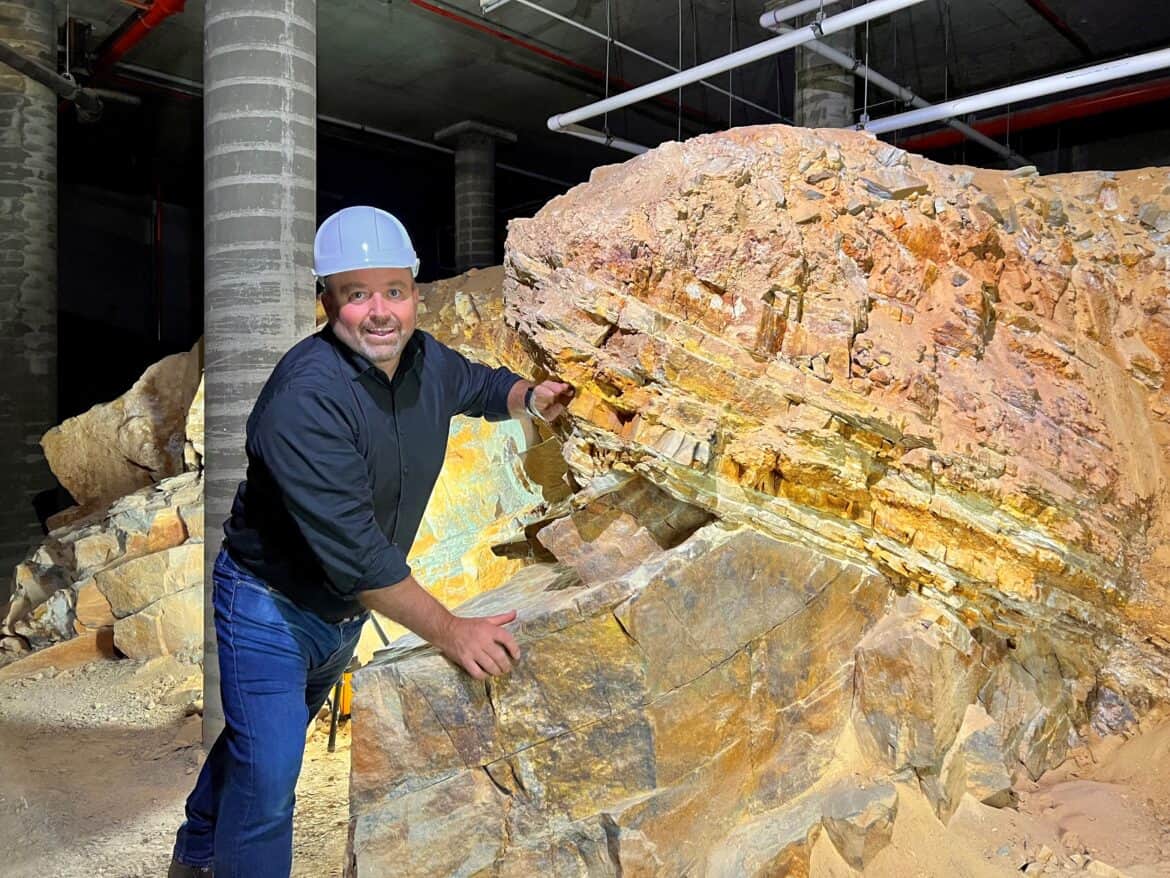 Photo of man (Dr Steve Hill of Geoscience Australia)in a hard hat examining a large rock - a geological unconformity under eh Australian Parliament House