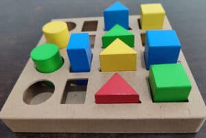 Photo of a shape sorter toy half-filled with colourful shapes in green, blue, yellow and red