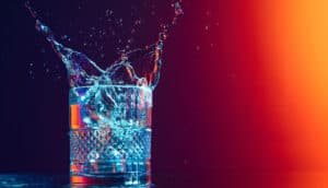 Digital image of ice being dropped into a whisky glass against a red-glowingbackground. Image by Master 1305 at Shuttlestock