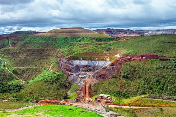 View of Vale's Itabirito mine in Minas GErais, Brazil, an opencast stope mine set in a hillside against green vegetation and blue sky. Image by rocharibeiro at Shutterstock.