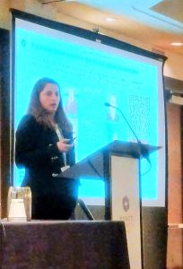 Carolina Frey, a woman with dark hair speaking at a lectern in front of a screen