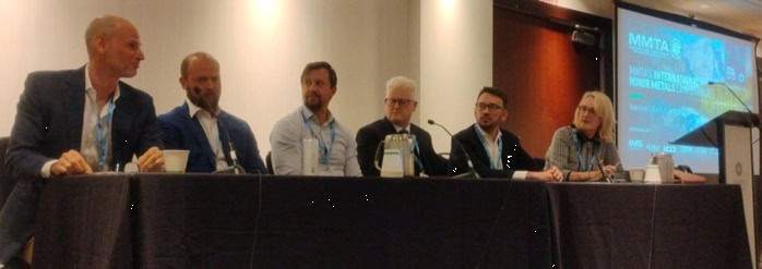 MMTA Panel of five men and one woman sitting at a conference table with a screen in the background.