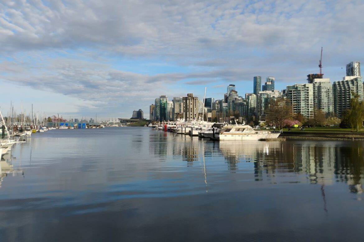 View of Vanccouver city waterfront with water, cloudy sky, boats, buildings, trees.